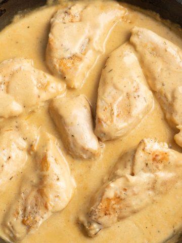 Creamy honey mustard sauce surrounding cooked chicken breasts in a cast-iron skillet.
